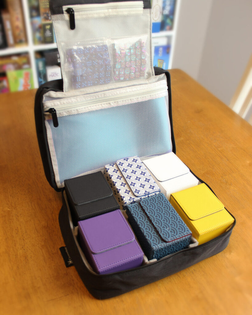 The Keep bag on the table with 6 different deck boxes and other components in the mesh zipper pockets.